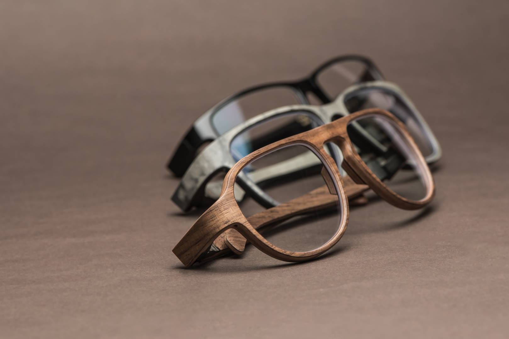 Drei Rolf Hornbrillen mit feiner Maserung und elegantem Design, präsentiert auf braunem Untergrund, symbolisieren Qualität und Handwerkskunst.